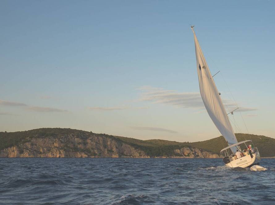 Yate a vela navegando cerca de la costa al atardecer